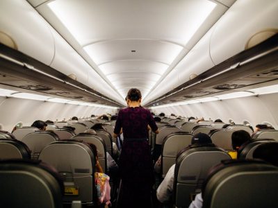 pexels-photo-3119978 Interior view of an airplane cabin with passengers seated and a flight attendant walking down the aisle.
